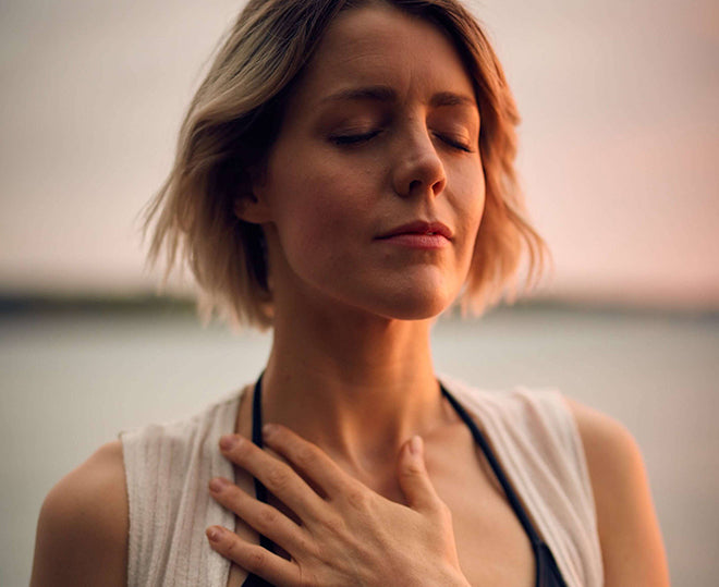 Woman calming herself by the oceanside holding her heart